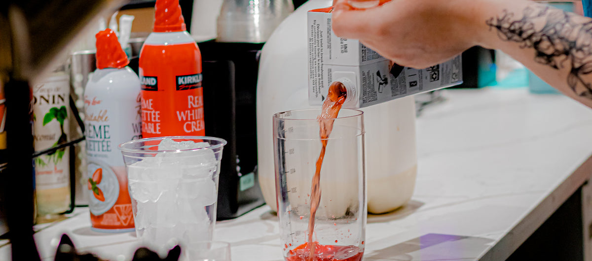 person pouring red liquid in a measuring cup besides a cup full of ice cubes