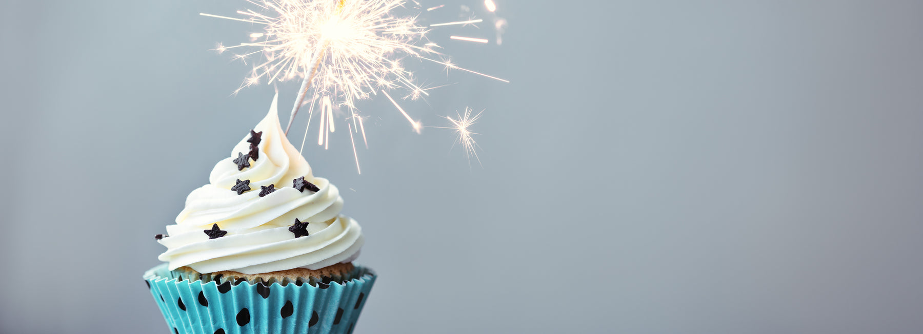 cupcake with white icing, black star toppings, and a sparkler